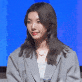 a woman wearing a grey jacket and a necklace has a microphone on her neck
