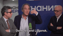three men are standing in front of a blue sign that says donbass and lugansky