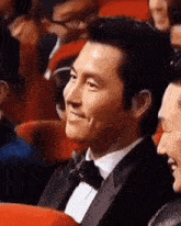 a man in a tuxedo is smiling while sitting in a crowd of people .