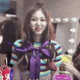 a woman in a striped shirt with a purple bow around her neck stands in front of a mirror
