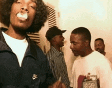 snoop dogg is smoking a cigarette while standing next to a group of men in a room .