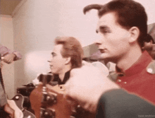 a man in a red shirt is playing a guitar in a band