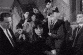 a black and white photo of a group of people standing around a woman in a room .