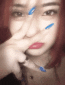 a woman with red hair and blue nails is making a peace sign with her fingers