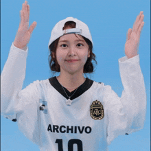 a woman wearing a white archivo 10 jersey with her hands in the air