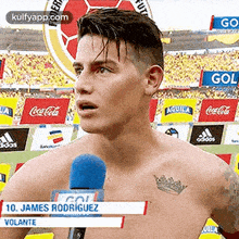 a shirtless man with a tattoo on his chest is talking into a microphone on a soccer field .