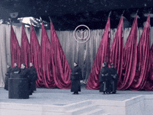 a group of people standing in front of a stage with red curtains behind them