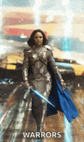 a woman in armor is holding a sword and a cape .