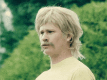 a man with blonde hair and a mustache is wearing a yellow shirt and earrings