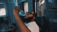 a man drinking from a bottle with a poster on the wall behind him that says ' i love you ' on it