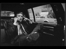 a man in a suit is talking on a phone in a car
