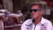 a man wearing sunglasses and a microphone is sitting in front of a vehicle .