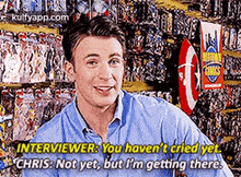 a man in a blue shirt is sitting in front of a wall of comics and talking to an interviewer .