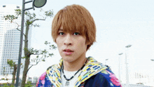 a young man wearing a necklace and a colorful jacket looks at the camera