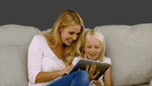 a mother and daughter are sitting on a couch looking at a tablet