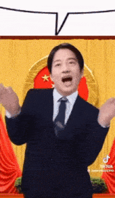 a man in a suit and tie is standing in front of a yellow curtain and making a funny face .