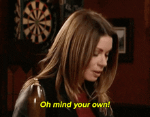 a woman is standing in front of a dart board and saying oh mind your own