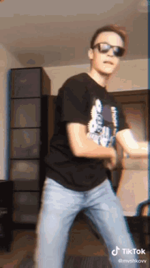a man wearing sunglasses and a black shirt is dancing in a living room .