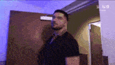 a man in a black shirt is standing in a hallway with a blue light behind him