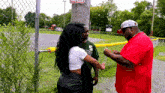 a man in a green shirt with the letter s on it is talking to a woman and a man in a red shirt .