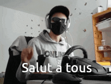 a man wearing a mask and headphones says salut a tous while sitting at a desk