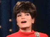 a woman is singing into a microphone while wearing a red sweater .
