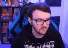 a man wearing glasses is sitting in a blue chair .