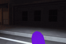 a purple object is standing in front of a dark building