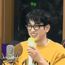 a man wearing glasses is smiling while holding a microphone in front of a microphone .