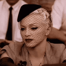 a woman with a veil on her face is wearing a hat and gloves