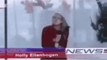 a woman is standing in front of a news desk with holly ellenbogen on it .