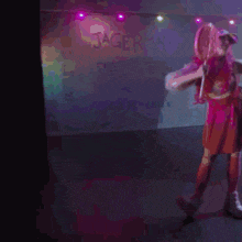 a woman in a pink dress is dancing on a stage in front of a wall that says jagerm