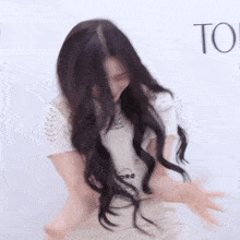 a woman with long dark hair is standing in front of a white wall with her arms outstretched .