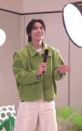 a man in a green jacket is holding a microphone in front of a light