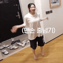 a woman in a white t-shirt and black shorts is standing in front of a door with a bunch of shoes on the floor