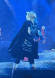a man in a black cape stands on a stage with a woman in a red dress behind him