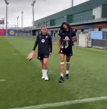 two women walking on a soccer field with one wearing a shirt that says ' spotify ' on it