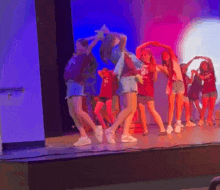 a group of young girls are dancing on a stage with purple lights behind them .