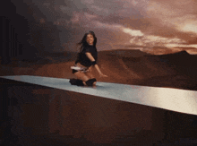 a woman is kneeling down on a ledge in the desert
