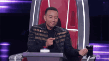 a man is sitting in a chair with the word the voice on the bottom right