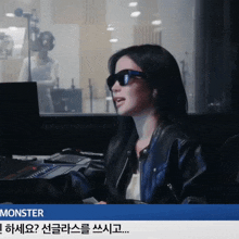 a woman wearing sunglasses and a leather jacket is sitting in front of a monitor with the word monster on the bottom