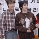 a man in a plaid shirt stands next to another man in a sweater