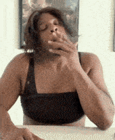 a woman in a black bra is sitting at a table and smoking a cigarette