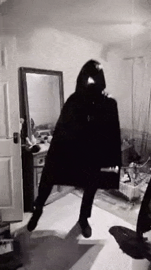 a black and white photo of a person in a black cape standing in a room .