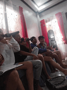 a group of people are sitting in a room with red curtains and a mirror