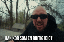 a man wearing sunglasses and a black hoodie says han kör som en riktig idiot