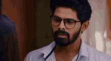 a man with a beard wearing glasses and a white shirt is talking to another man .