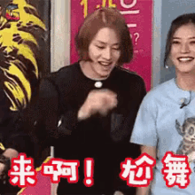 two women are standing next to each other in front of a sign with chinese writing on it .