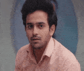 a man in a pink shirt looks at the camera with a surprised look on his face