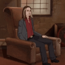 a man in a suit and red shirt is sitting in a brown chair